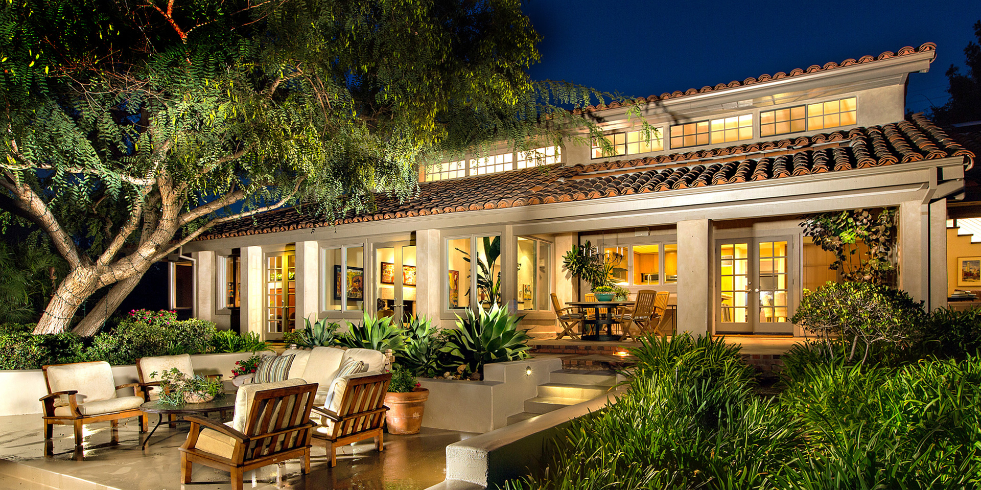 Rancho Santa Fe area estate at dusk with lit interiors, covered terrace and mature grounds
